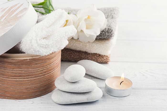 Set of bathroom accessory on wooden background: pebbles, towels, candle